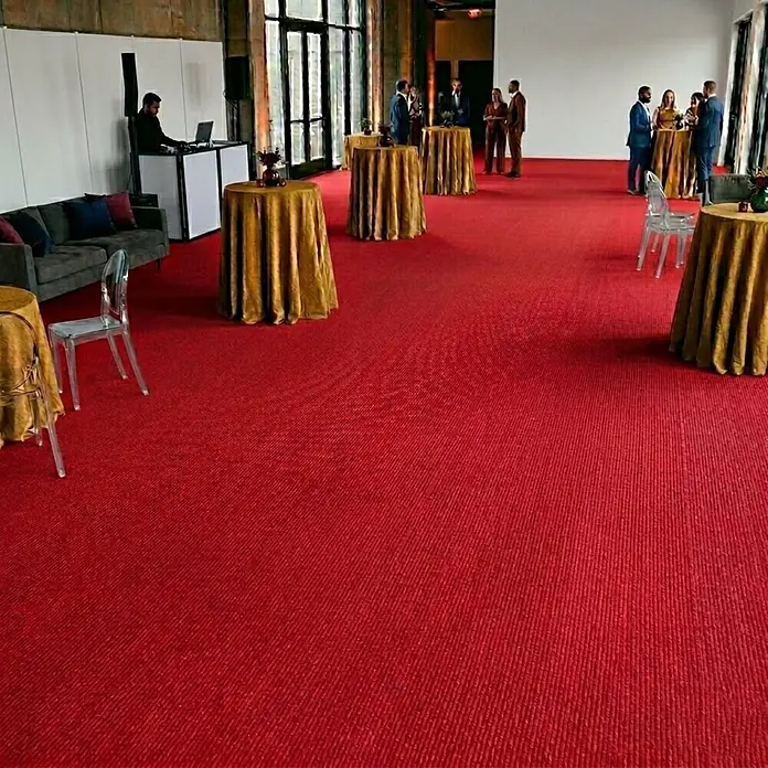 Floordirekt Teppichboden Meterware Sintra - für Messe & Events - Rot - 100 x 150 cm - Breite: 100 cm, Flachgewebe, Polypropylen, Rot - Großer roter gerippter Teppich bedeckt den Boden eines Veranstaltungsraums mit Personen und Möbeln.