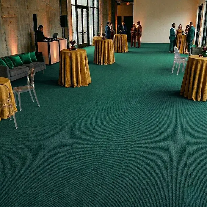 Floordirekt Teppichboden Meterware Sintra - für Messe & Events - Grün - 100 x 400 cm - Breite: 100 cm, Flachgewebe, Polypropylen, Grün - Dunkelgrüner gerippter Teppich in einer geräumigen Veranstaltungshalle mit Gästen und Tischen.