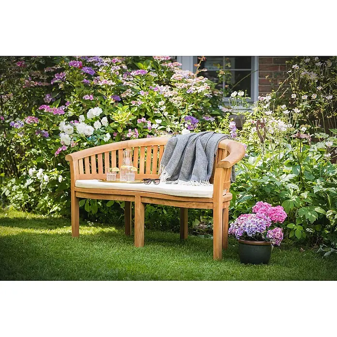 Kai Wiechmann Bankauflage - Kai Wiechmann Bananenbank, 1 Stk., L x B x H: 49 x 139 x 5 cm, 100% Acryl, Dralon®, naturweiß / cremeweiß - Gartenbank aus Holz mit cremefarbenem Kissen, grauer Decke, Getränken und Sonnenbrille in einer üppigen Gartenumgebung.
