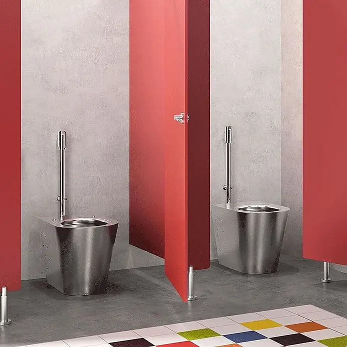 Delabie Stand-WC Delabie - Edelstahl - Zwei Edelstahltoiletten in öffentlichen Toilettenkabinen mit roten Trennwänden installiert.