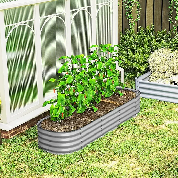Outsunny Hochbeet - Metall, Silber - Langes, gewelltes Hochbeet aus verzinktem Stahl mit Erde und Chilipflanzen neben einem Gewächshaus.