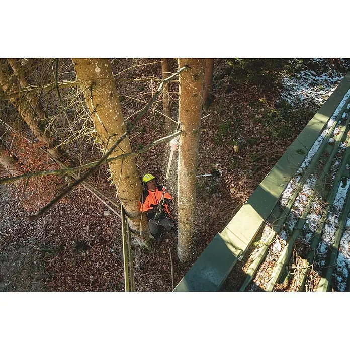 Metabo Hochentaster-Aufsatz - Passend für: Metabo Akku-Multifunktionsantrieb MA 36-18 LTX BL Q - Baumpfleger in oranger Jacke und gelbem Helm beschneidet Baum mit Kettensäge, Sägespäne fliegen.
