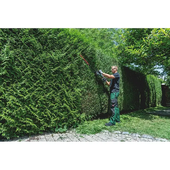 Metabo CAS 18V Akku-Heckenschere HS 18 LTX BL 55 - 18 V, Schnittlänge: 50 cm - Mann in grüner Hose schneidet mit einer grün-schwarzen Heckenschere eine große Hecke.