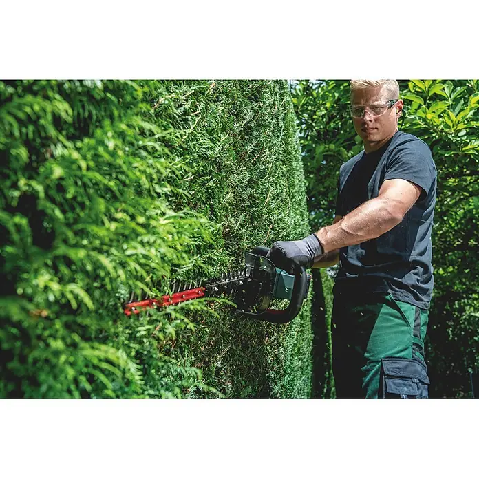 Metabo CAS 18V Akku-Heckenschere HS 18 LTX BL 75 - 18 V, Ohne Akku, Schnittlänge: 70 cm - Mann in Schutzbrille und Handschuhen schneidet eine grüne Hecke mit einer Heckenschere.