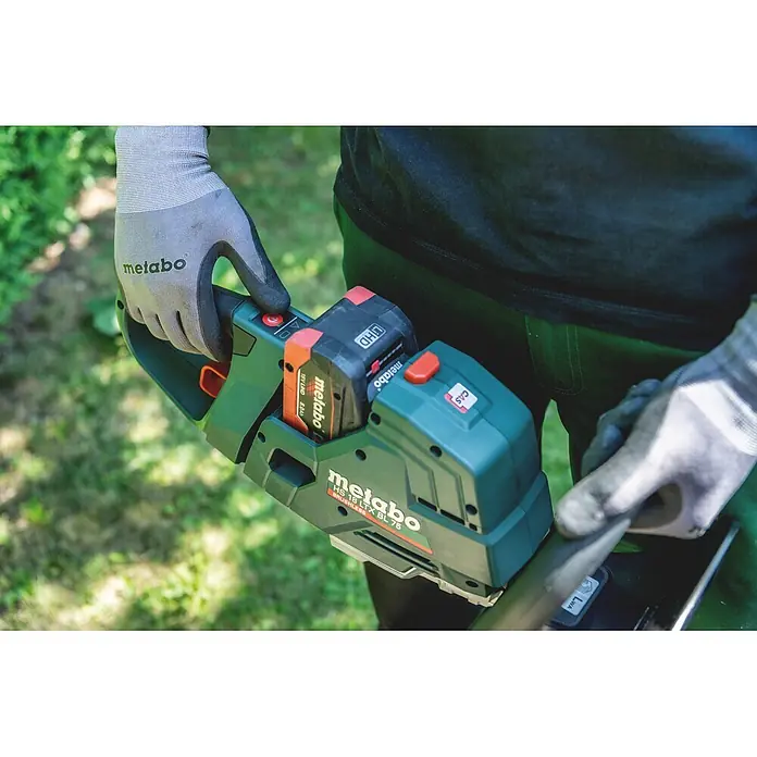 Metabo CAS 18V Akku-Heckenschere HS 18 LTX BL 55 - 18 V, Schnittlänge: 50 cm - Person in Handschuhen hält eine grüne und schwarze Metabo Akku-Heckenschere mit 18V LiHD Akku, bereit für den Garten.