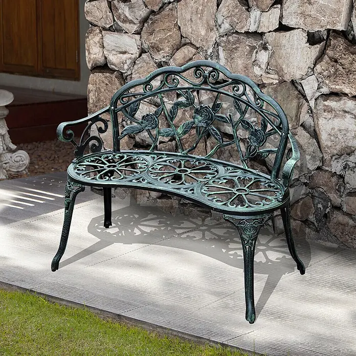 Outsunny Gartenbank - Gussaluminium, Gusseisen, Antik Grün - Verzierte dunkelgrüne Metall-Gartenbank mit Rosen- und Blattmuster, auf einer Terrasse vor einer Steinmauer.