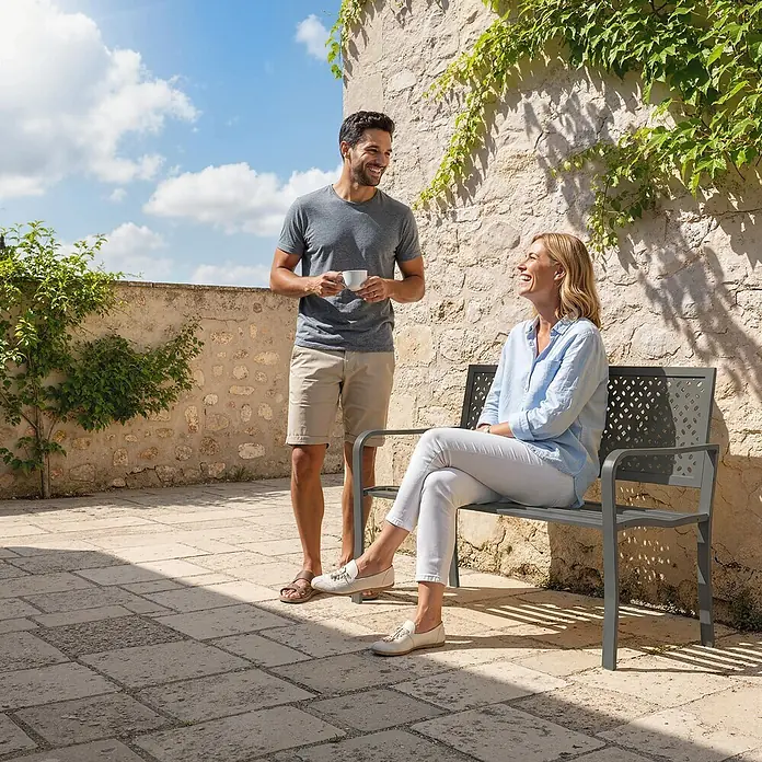 Furnicato Gartenbank pulverbeschichtet - B x T x H: 61 x 127 x 85 cm, Stahl, Dunkelgrau - Dunkelgraue Metallgartenbank mit gemusterter Rückenlehne, auf der eine Frau auf einer sonnigen Terrasse sitzt.