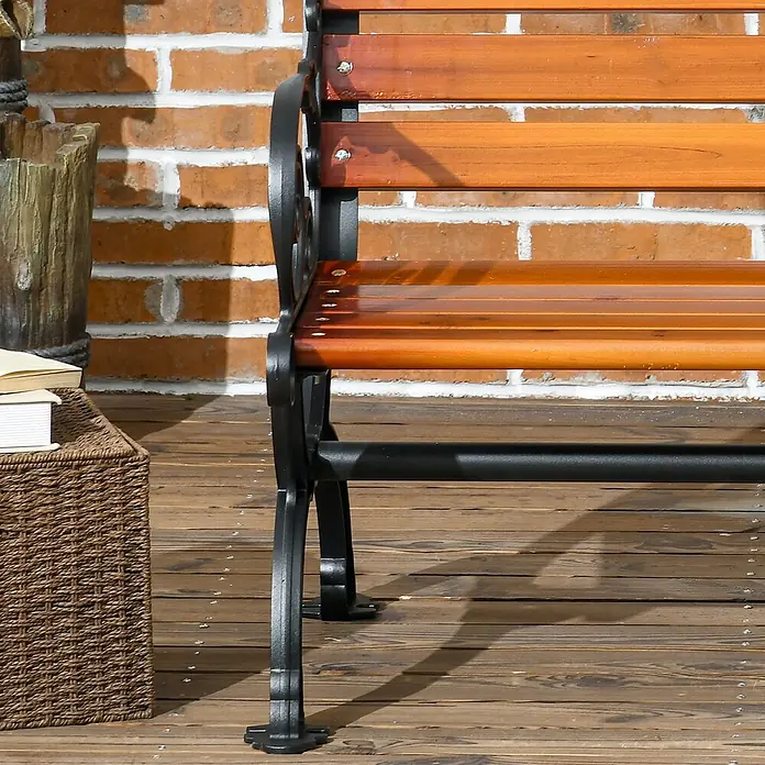 Furnicato Gartenbank - Aluminium/Holz, Teak - Eine braune Holz-Gartenbank mit schwarzem Gusseisengestell steht auf einer Holzterrasse vor einer Ziegelwand.