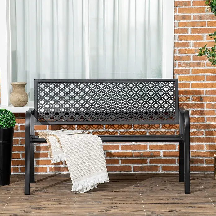 Outsunny Gartenbank - B x T x H: 63 x 63 x 83 cm, Stahl, Schwarz - Schwarze Metall-Gartenbank mit gemusterter Rückenlehne auf Holzterrasse, mit heller Decke drapiert.