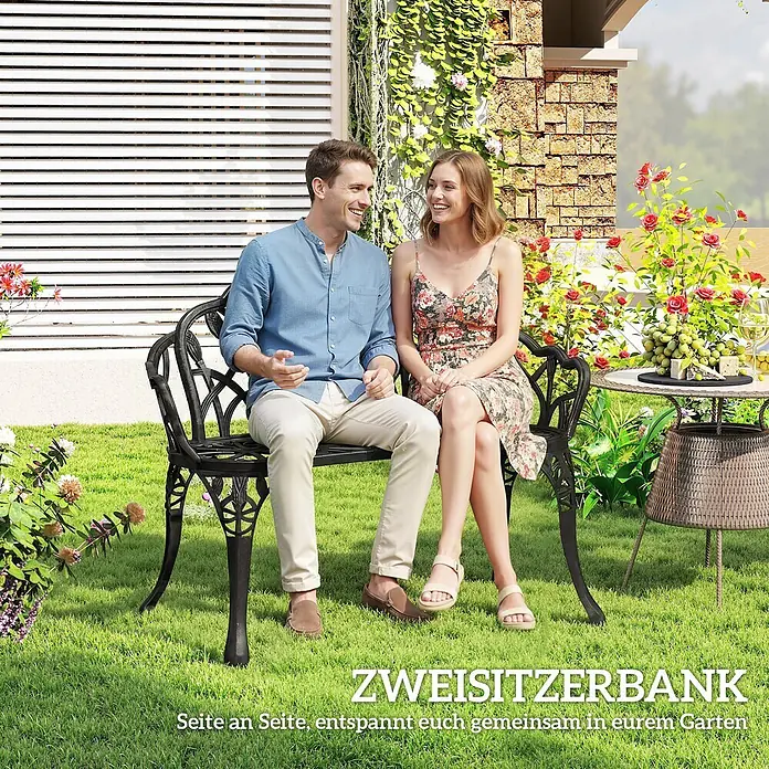 Outsunny Gartenbank - Aluminiumguss, Schwarz - Verzierte dunkle Metallguss-Zweisitzer-Gartenbank mit einem Paar, das sich in einem Garten entspannt.