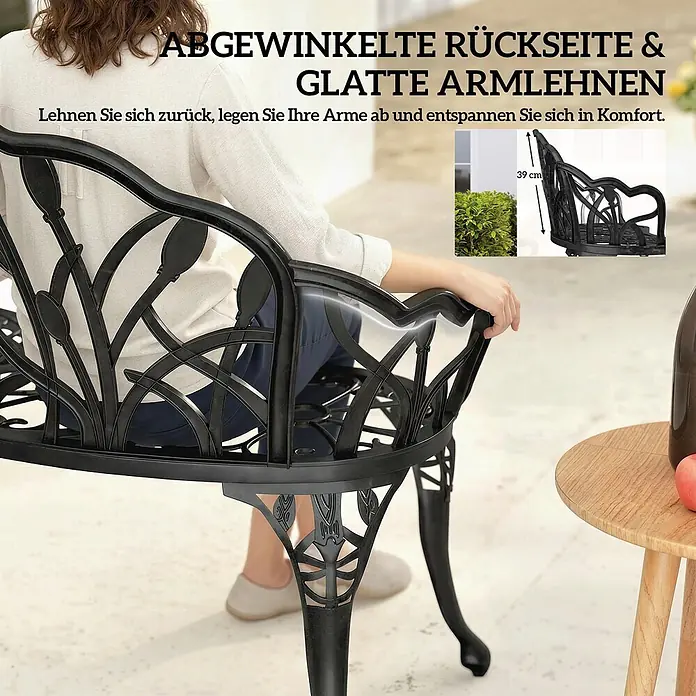 Outsunny Gartenbank - Aluminiumguss, Schwarz - Schwarze Gartenbank aus Gusseisen mit angewinkelter Rückenlehne, botanischem Muster und glatten Armlehnen, eine Person entspannt darauf.
