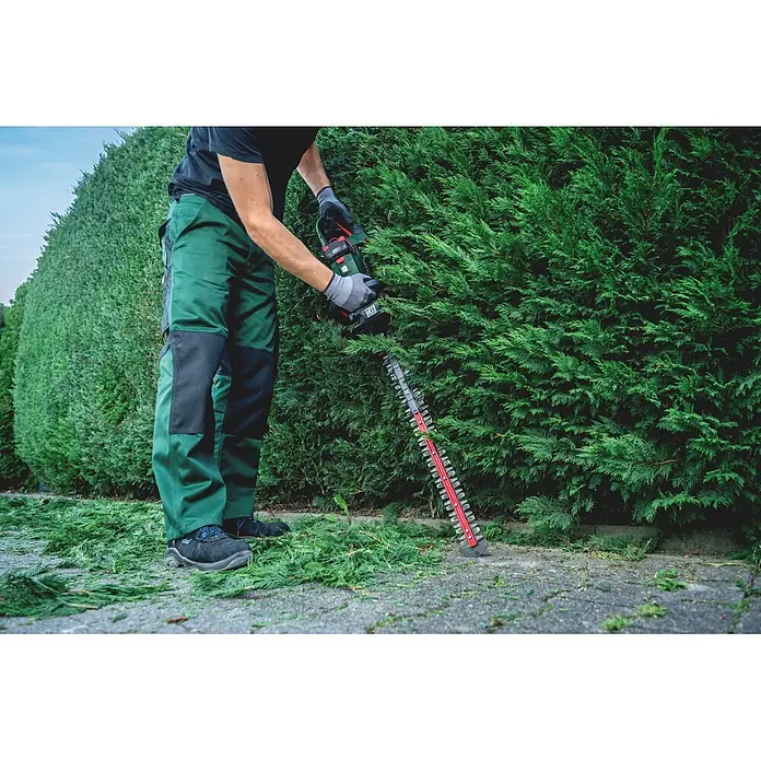 Metabo CAS 18V Akku-Heckenschere HS 18 LTX BL 65 - 18 V, Ohne Akku, Schnittlänge: 60 cm - Person schneidet mit einer grün-schwarzen Heckenschere mit roten und silbernen Klingen Laubwerk.