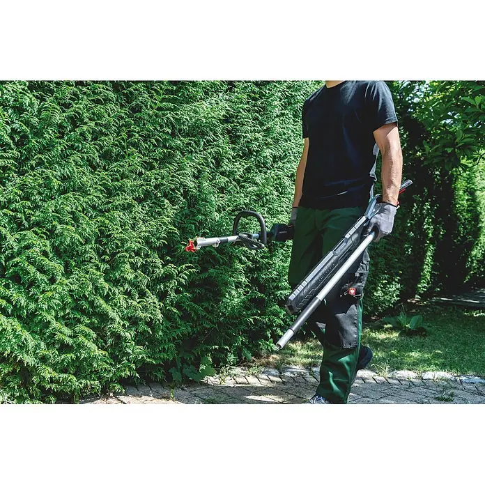 Metabo Heckenscheren-Aufsatz - Passend für: Akku-Multifunktionsantrieb MA 36-18 LTX BL Q - Eine Person trägt ein schwarzes und silbernes Metabo Gartengerät mit roter Spitze, bereit für den Einsatz an einer Hecke.