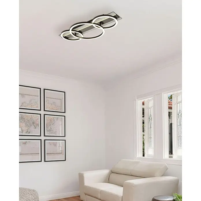 Globo LED-Deckenleuchte Norberto - 40 W, L x B x H: 622 x 300 x 88 mm, Neutralweiß - Schwarze Deckenleuchte mit drei überlappenden beleuchteten Ringen, über einem cremefarbenen Sofa im Wohnzimmer.
