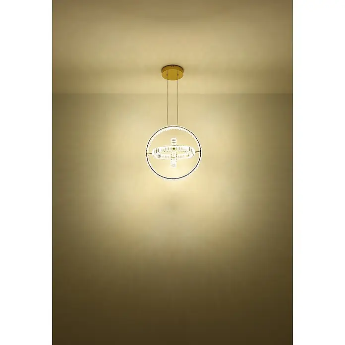 Globo LED-Pendelleuchte rund Neil - 115 W, Höhe: 1.300 mm - Beleuchteter runder Kristall-Kronleuchter mit goldener Deckenhalterung in einem warm getönten Raum.