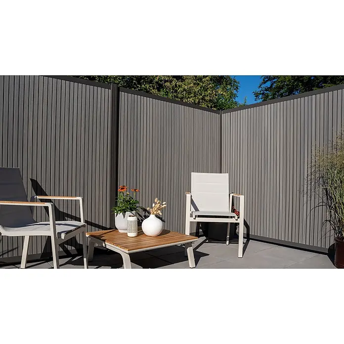 GartenLand Steckzaun-Element WPC Zaun Shadowline Vertikal Ohne Pfosten - Amethystgrau, Verbundwerkstoff - Grauer Lamellen-Sichtschutz aus Verbundmaterial, bildet eine Ecke für eine Terrassensitzgruppe.
