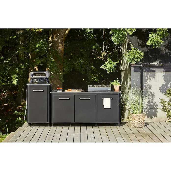 Cozze Outdoorküchen-Modul - Schwarz, B x T x H: 180 x 60 x 90 cm - Dunkelgraue modulare Außenküche mit Pizzaofen und Gaskochfeld auf Holzterrasse umgeben von Bäumen.