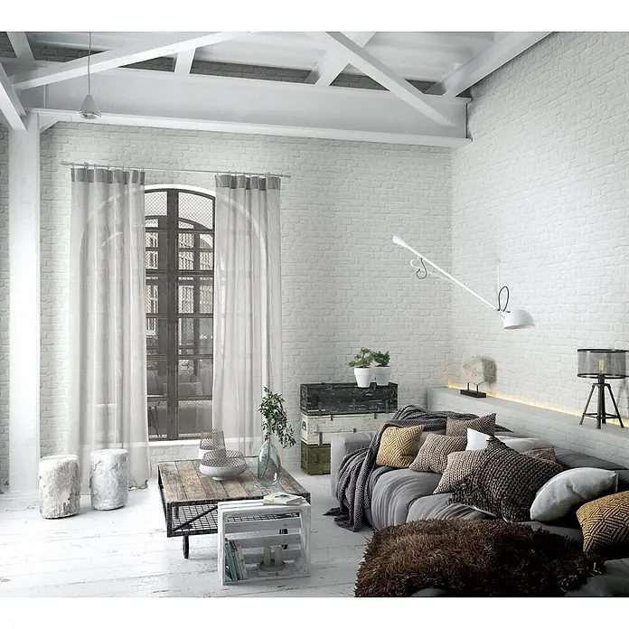 Marburg Loft Superior Vliestapete Steinoptik - Weiß, Steinoptik, 10,05 x 0,53 m - Ein Wohnzimmer im Industrial-Chic mit weißen Ziegelwänden, einem grauen Sofa mit strukturierten Kissen und rustikalen Holzmöbeln.
