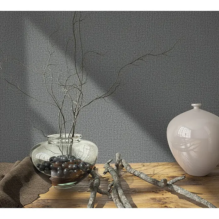 Vliestapete - Anthrazit, Sonstiges, 10,05 x 0,53 m - Eine klare Glasvase mit kahlen Ästen und dunklen Dekokugeln, eine hellbeige Keramikvase und knorrige Äste auf einem Holztisch mit braunem Stoff.