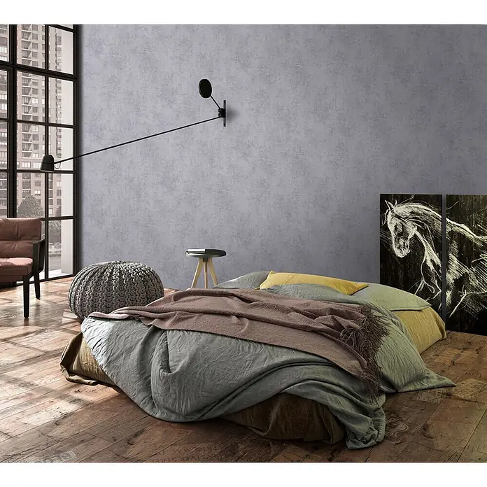 Marburg Loft Superior Vliestapete Struktur I - Steingrau, Sonstiges, 10,05 x 0,53 m - Ein gemütliches Schlafzimmer mit einem niedrigen Bett, geschichteter grüner, brauner und rosa Bettwäsche sowie einem gelben Kissen auf rustikalem Holzboden.