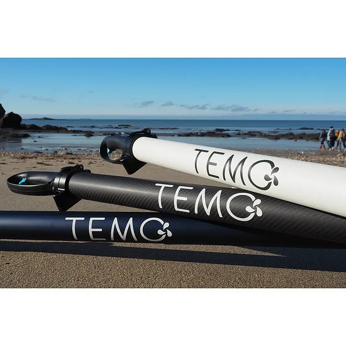 Temo Elektro-Außenbordmotor 450 Nacre-Edition - 450 W, Pinnensteuerung - Drei TEMO Elektromotoren (weiß, Carbon schwarz, dunkelblau) mit Griffen, gestapelt am Sandstrand am Meer.