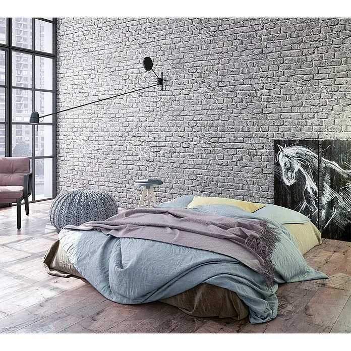 Marburg Loft Superior Vliestapete Steinoptik - Taupe, Steinoptik, 10,05 x 0,53 m - Weiße, strukturierte Ziegelwand in einem modernen Schlafzimmer mit niedrigem Bett, großem Fenster und Strickpouf.