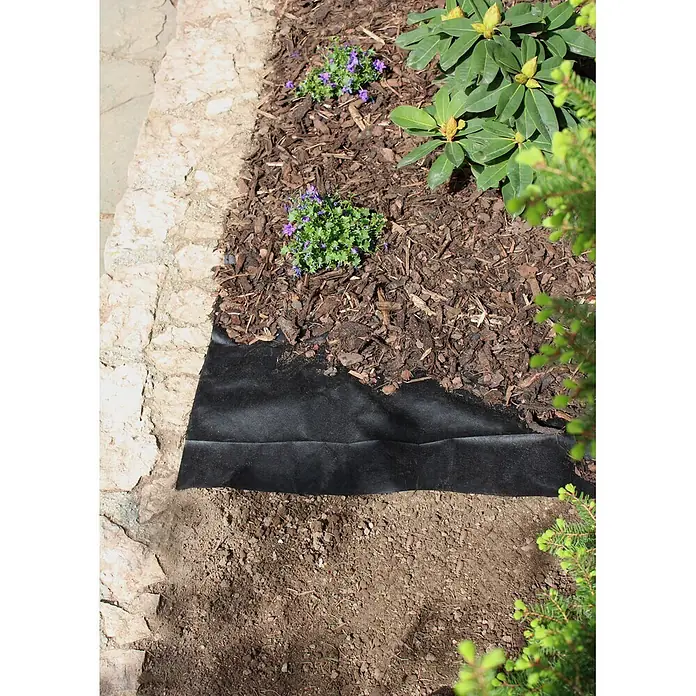 Windhager Unkrautvlies - Vlies, 10 x 0,9 m - Schwarzes Gartenvlies auf nackter Erde, grenzt an ein gemulchtes Blumenbeet mit Pflanzen.
