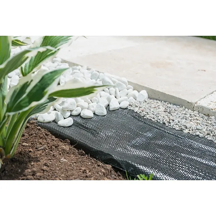 Windhager Unkrautabwehrgewebe Unterboden-Gewebe - Vlies, 25 x 2 m - Schwarzes Unkrautvlies im Garten verlegt, teils mit weißen Ziersteinen bedeckt, neben Erde und Pflanze.