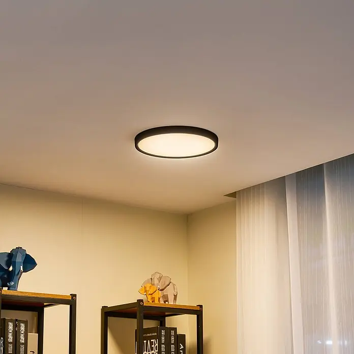 Lindby Deckenleuchte Pravin - schwarz - Eine runde Deckenleuchte mit schwarzem Rahmen und weißem Diffusor beleuchtet einen modernen Raum.