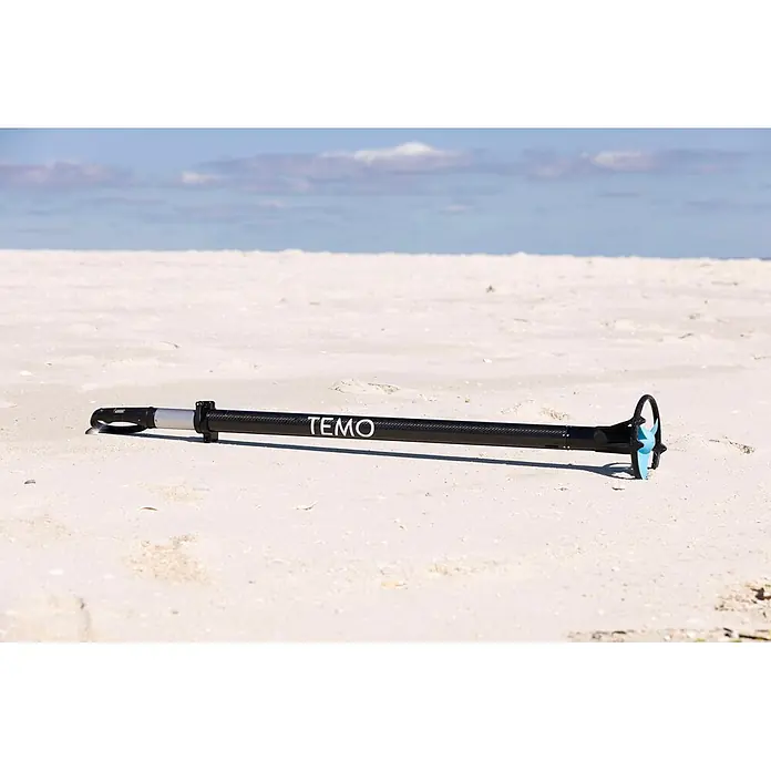 Temo Elektro-Außenbordmotor 450 Carbon - 450 W, Pinnensteuerung - Schwarzer tragbarer Elektromotor mit Carbon-Schaft und hellblauem Propeller, liegt an einem Sandstrand.