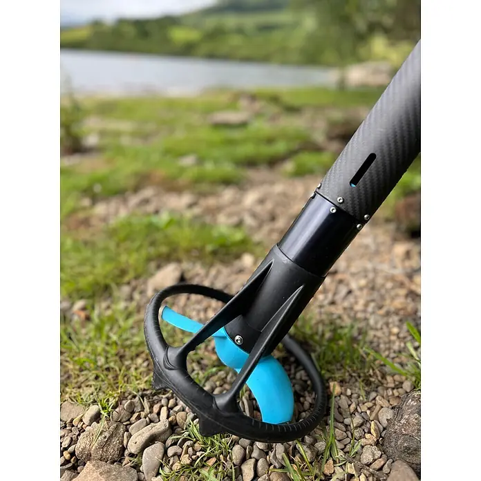 Temo Elektro-Außenbordmotor 450 Carbon - 450 W, Pinnensteuerung - Schwarzer Kohlefaserstab mit schwarzem Gehäuse und blauem Propeller, auf steinigem Ufer am Wasser.