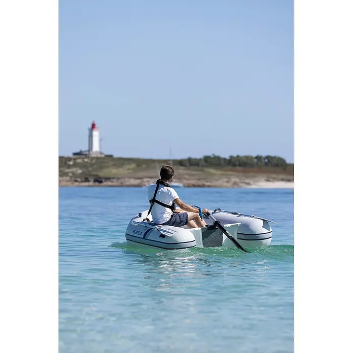 Temo Elektro-Außenbordmotor 450 Carbon - 450 W, Pinnensteuerung - Grau-weißes Schlauchboot mit einer Person, die in klarem, blauem Wasser auf einen Leuchtturm zu rudert.
