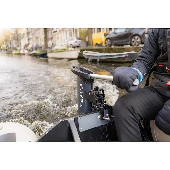 Temo Elektro-Außenbordmotor 1000 - 1.100 W, Pinnensteuerung - Person in einem Boot bedient einen dunkelgrauen TEMO Elektromotor mit silberner Welle, der Wellen im Wasser erzeugt.