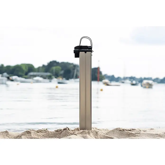 Temo Akku für Elektro-Außenbordmotor TEMO 1000 -  - Rechteckige Metallsäule mit schwarzem Oberteil, im Sand am Wasser vor Booten stehend.