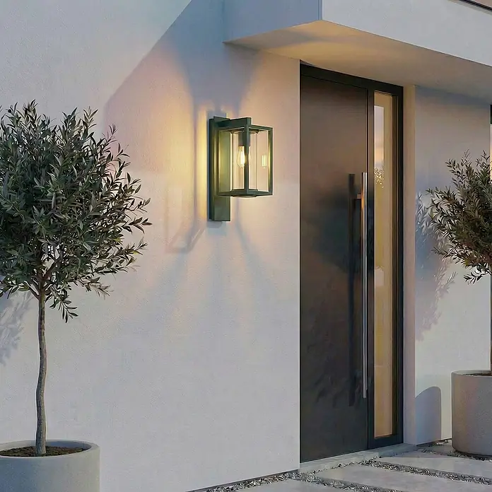 Lucande Außenwandleuchte Ferda - grün, grün, IP44 - Moderne dunkelgrüne Metall-Außenwandleuchte mit klaren Glaspaneelen, die eine Hausfassade neben einer Tür beleuchtet.