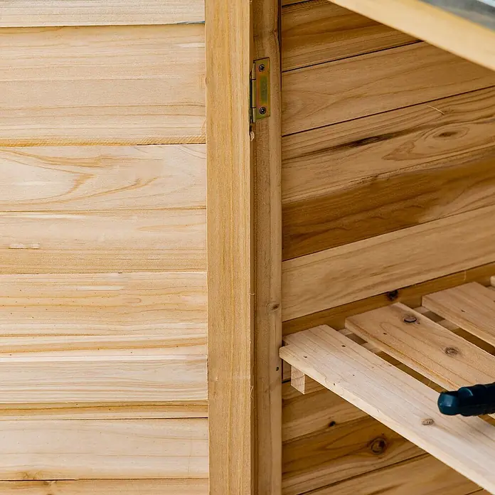 Outsunny Geräteschrank - Außenbreite inkl. Dachüberstand: 83 cm, Außentiefe inkl. Dachüberstand: 40 cm, Holz, Naturholz - Innenansicht eines hellen Holzschranks mit Lattenböden und einem sichtbaren Metallscharnier.