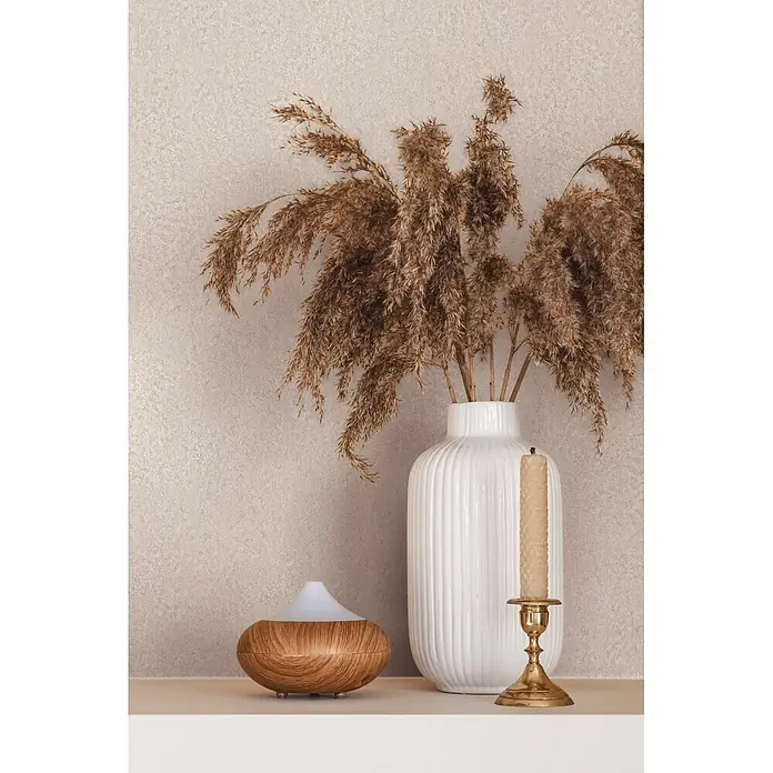 Marburg Ritus Vliestapete Putzoptik I - Creme, Sonstiges, 10,05 x 0,53 m - Ein Aroma-Diffusor mit Holzmaserung, eine weiße gerippte Vase mit getrocknetem Pampasgras und eine beigefarbene Kerze in einem Messinghalter auf einem Regal.