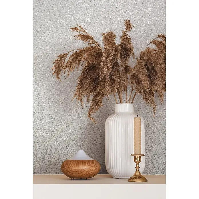Marburg Ritus Vliestapete Grafik II - Weiß, Grafisch, 10,05 x 0,53 m - Eine Ansammlung von Wohnaccessoires auf einem Regal: ein Holz-Aromadiffusor, eine weiße gerippte Vase mit getrocknetem Pampasgras und ein Messingleuchter mit Kerze.