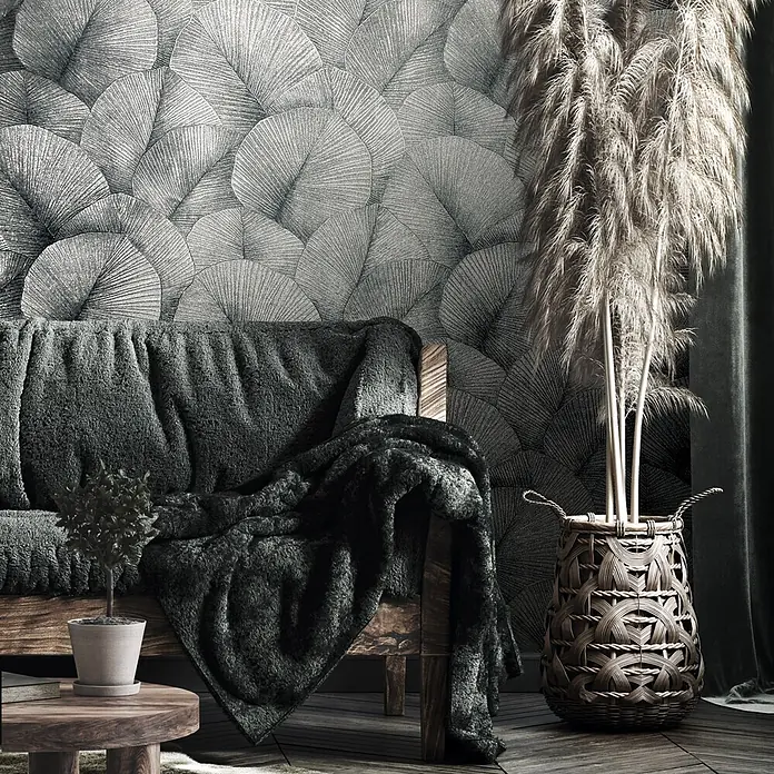 Marburg Kumano Vliestapete Floral - Silber, Floral, 10,05 x 0,53 m - Dunkelgraue Tapete mit überlappendem, fächerartigem Blattmuster an einer Wand, hinter einem Sofa und getrocknetem Pampasgras in einem Korb.