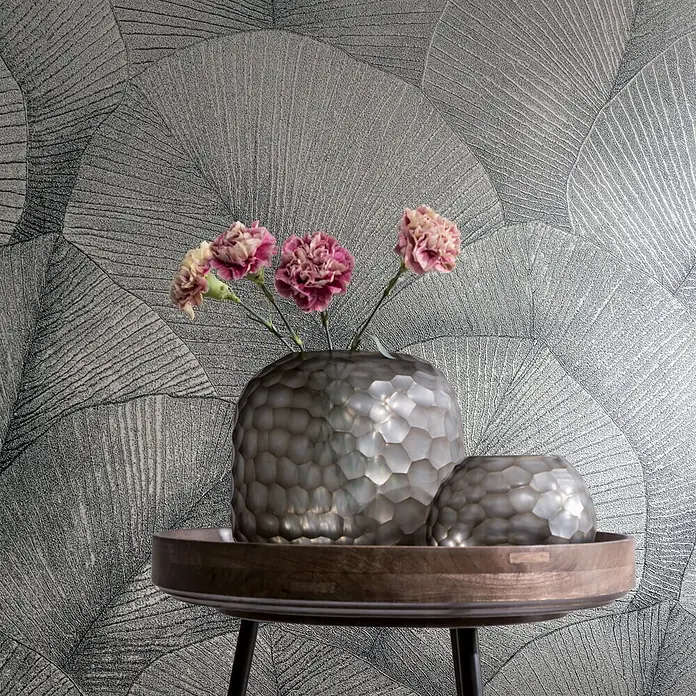 Marburg Kumano Vliestapete Floral - Silber, Floral, 10,05 x 0,53 m - Zwei metallische, wabenstrukturierte Vasen/Schalen mit Blumen auf einem Holztablett vor gemusterter Wand.