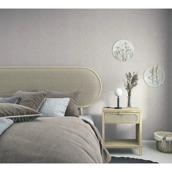 Marburg Boho Vliestapete Uni I - Braun, Uni, 10,05 x 0,53 m - Schlafzimmer mit geflochtenem Rattan-Kopfteil und passendem Nachttisch aus hellem Holz, kombiniert mit weicher, grauer Bettwäsche.