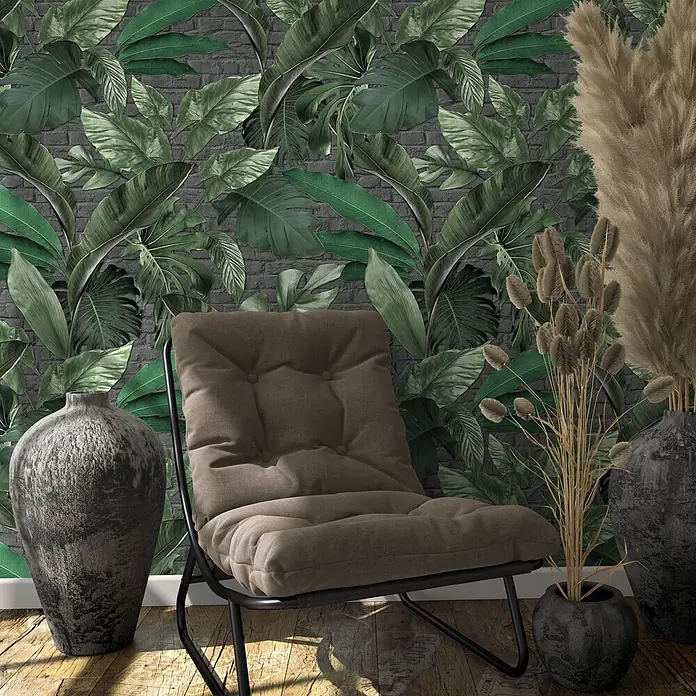 Marburg Loft Superior Fototapete Urban Jungle - B x H: 159 mm x 270 cm, Vlies, Grün-Graphit - Brauner gepolsterter Lounge-Sessel mit schwarzem Metallgestell, in einem Raum mit tropischer Blatttapete und Deko-Vasen.