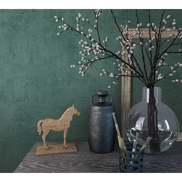 Marburg Loft Superior Vliestapete Struktur I - Grün, Sonstiges, 10,05 x 0,53 m - Weidenkätzchenzweige in einer klaren Glasvase, eine dunkle Metallurne, eine Holzpferdefigur und Pinsel in einem Halter auf einem Holztisch.