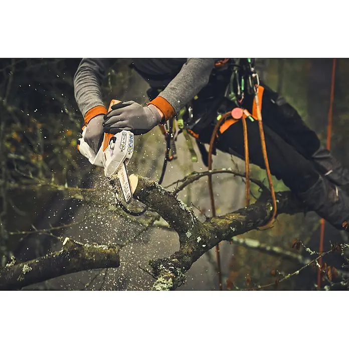 Stihl Führungsschiene - Passend für: Stihl Akku-Gehölzschneider GTA 30 und STIHL GTA 40 - Ein Baumpfleger in Kletterausrüstung verwendet eine weiß-orange Stihl Kettensäge, um einen Ast zu sägen, wobei Sägespäne entstehen.