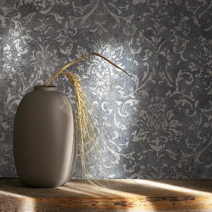 Marburg City Glow Vliestapete Ornamental - Schwarz-Silber, Ornament, 10,05 x 0,53 m - Eine matte graue Vase mit getrockneten Weizenähren steht auf einem rustikalen Holzregal vor einer gemusterten Wand.
