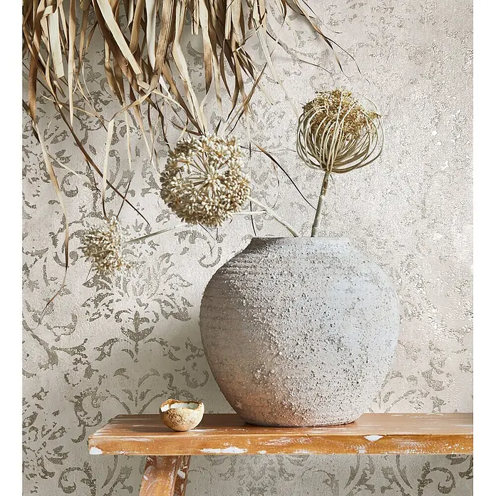 Marburg City Glow Vliestapete Ornamental - Beige, Ornament, 10,05 x 0,53 m - Strukturierte beigefarbene Tapete mit goldenem Zier­muster, in gemütlicher Umgebung mit rustikaler Vase und Trockenpflanzen.