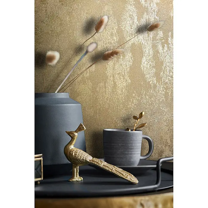 Marburg City Glow Vliestapete Struktur - Gold, Sonstiges, 10,05 x 0,53 m - Goldene Vogelfigur, dunkelgraue Vase mit Trockengras und gerippter Tasse auf einem Tablett vor einer goldstrukturierten Wand.