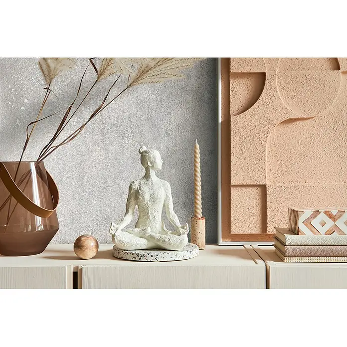 Marburg City Glow Vliestapete Uni I - Grau, 10,05 x 0,53 m - Weiße, texturierte Yoga-Statue auf gesprenkelter Basis, Teil einer friedlichen Deko-Anordnung auf hellem Schrank.
