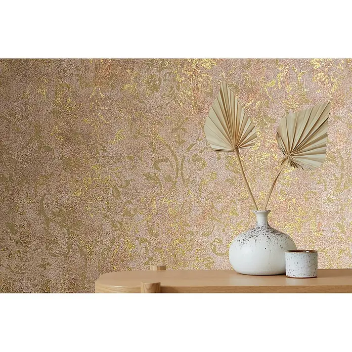 Marburg City Glow Vliestapete Ornamental - Braun-Gold, Ornament, 10,05 x 0,53 m - Goldene, strukturierte Tapete mit Mustern, an einer Wand hinter einem Tisch mit einer weißen Vase und Trockenblättern.