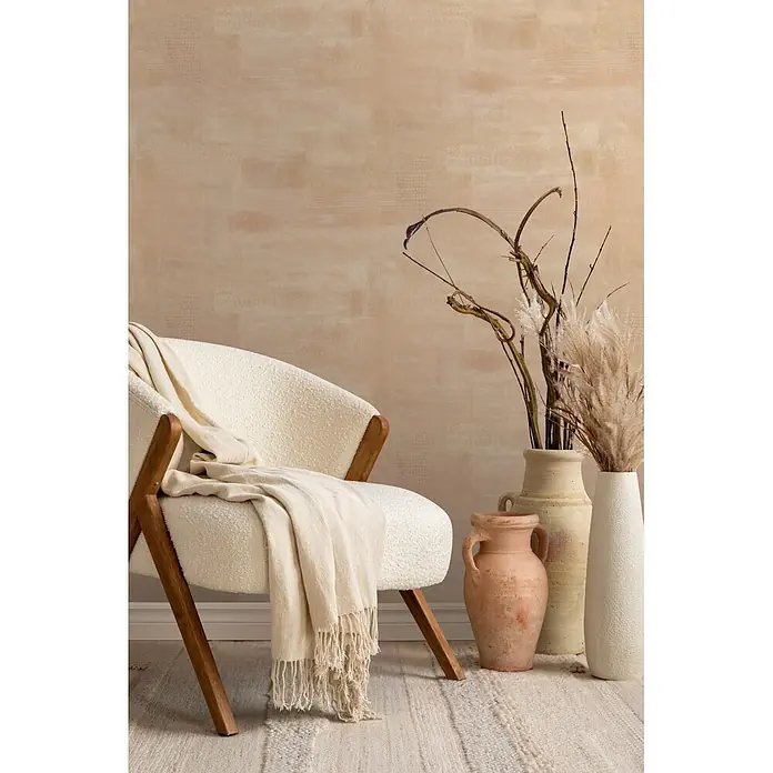 Marburg Novamur Plus Fresh UP Vliestapete Uni I - Beige, Uni, 10,05 x 0,53 m - Ein cremefarbener Sessel mit Holzbeinen und einer beigen Decke, platziert in einem gemütlichen Raum mit Deko-Vasen.